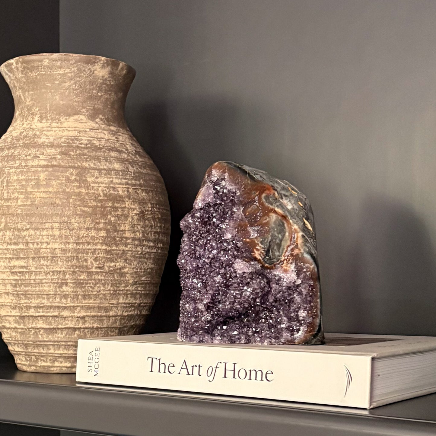 Purple amethyst crystal cluster styled on shelf with ceramic vase and design book