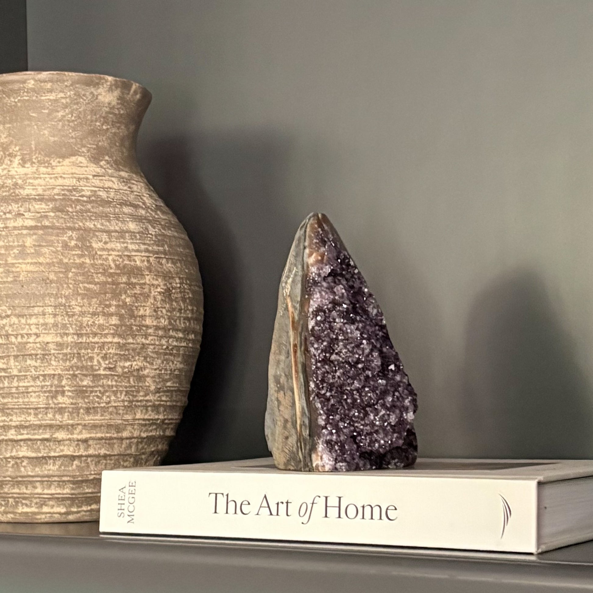 Amethyst cluster display on shelf with earthy vase and coffee table book