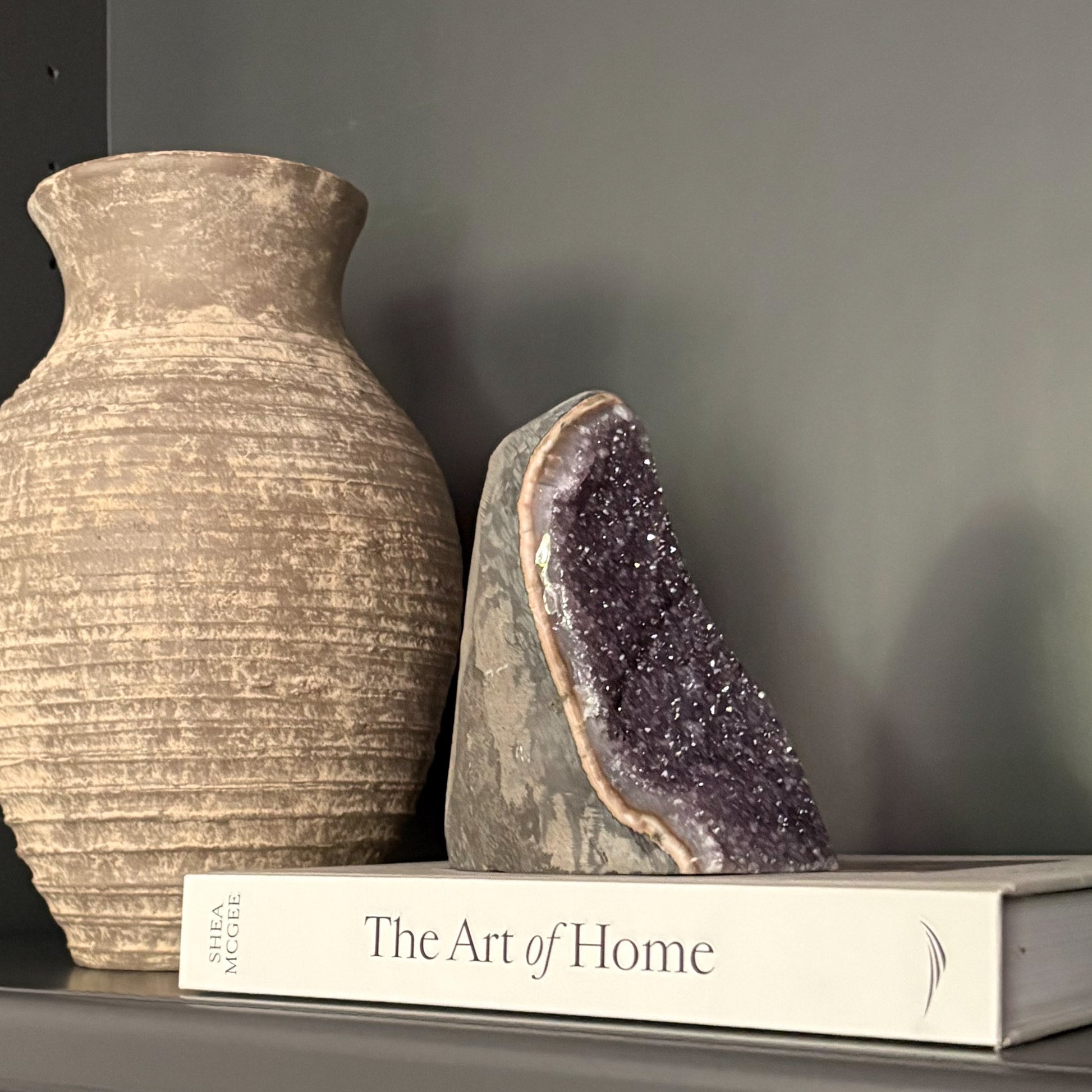 Amethyst cluster display on shelf with earthy vase and coffee table book