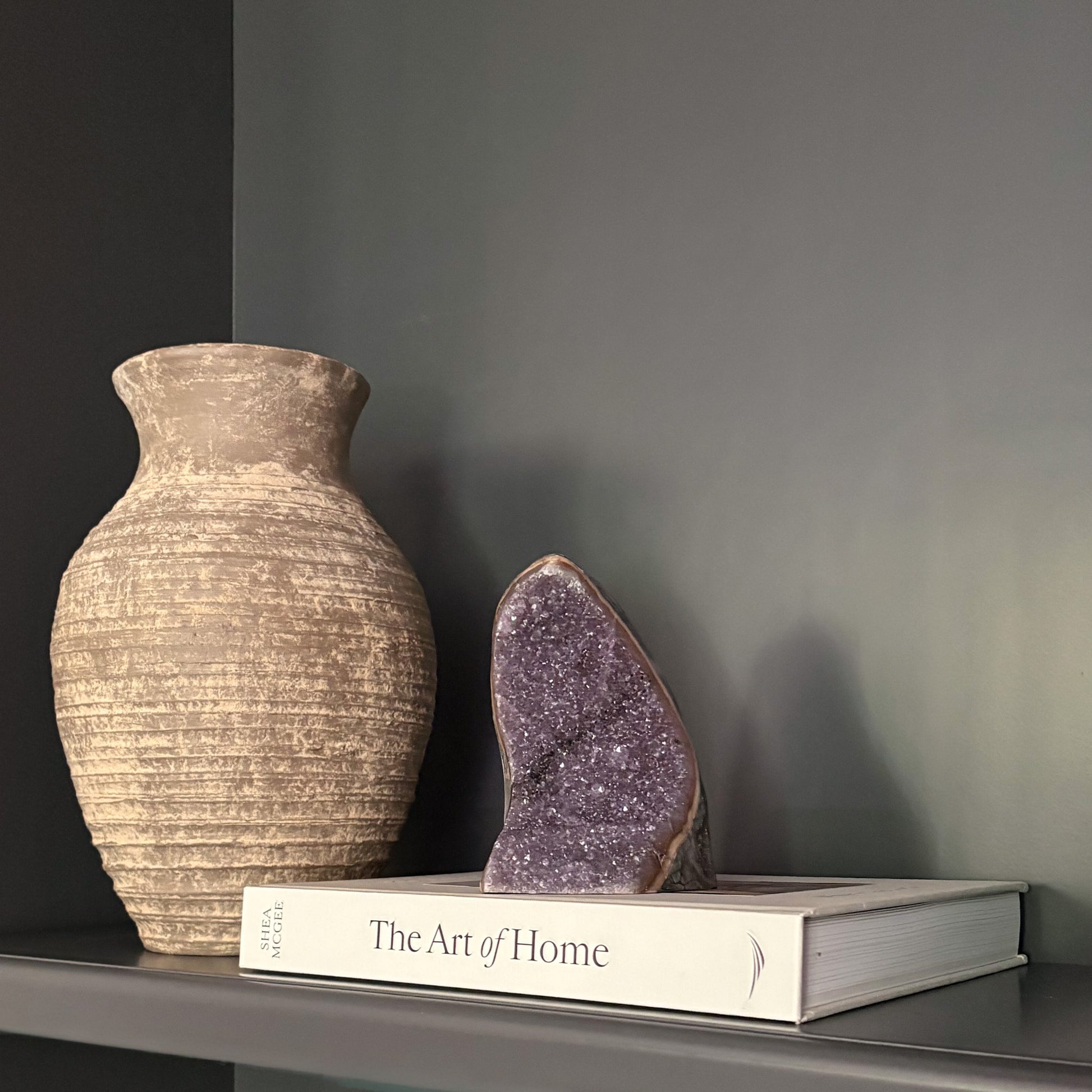 Purple amethyst crystal cluster styled on shelf with ceramic vase and design book