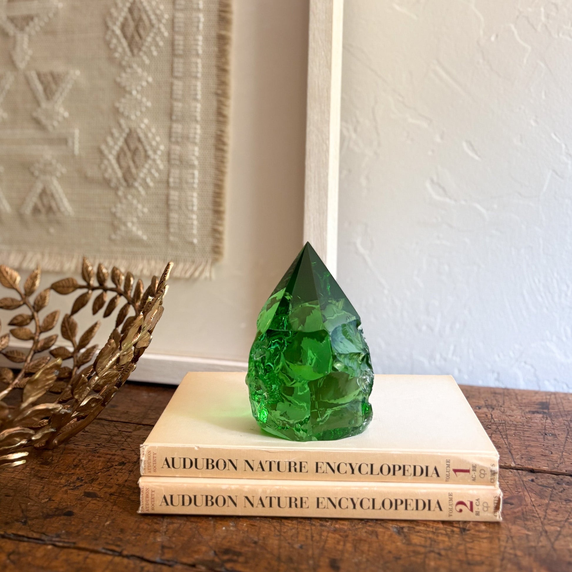 Green glass statue on top of two 'Audubon Nature Encyclopedia' books with a decorative wall in the background.