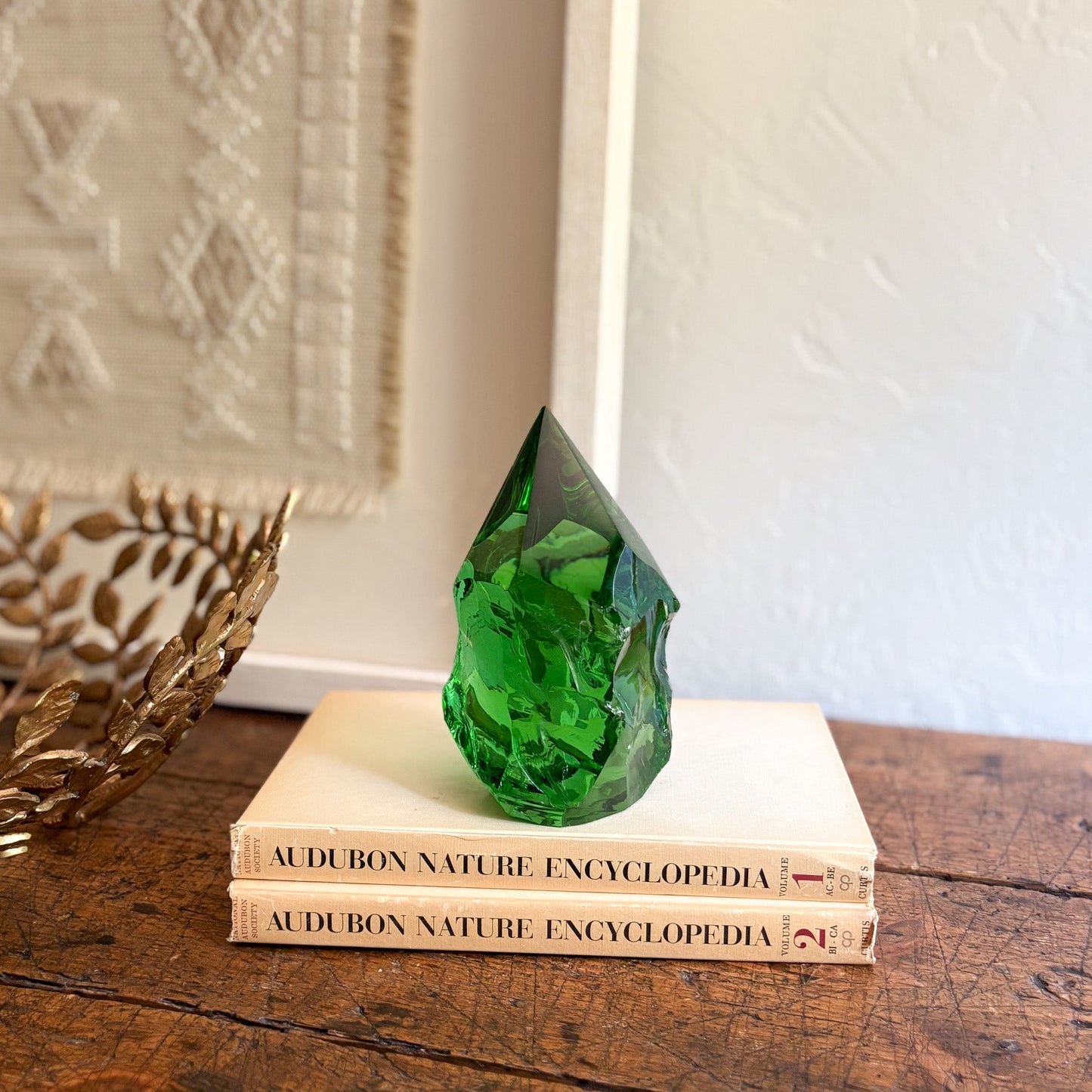 Green glass sculpture on top of two 'Audubon Nature Encyclopedia' books with a decorative wall in the background.