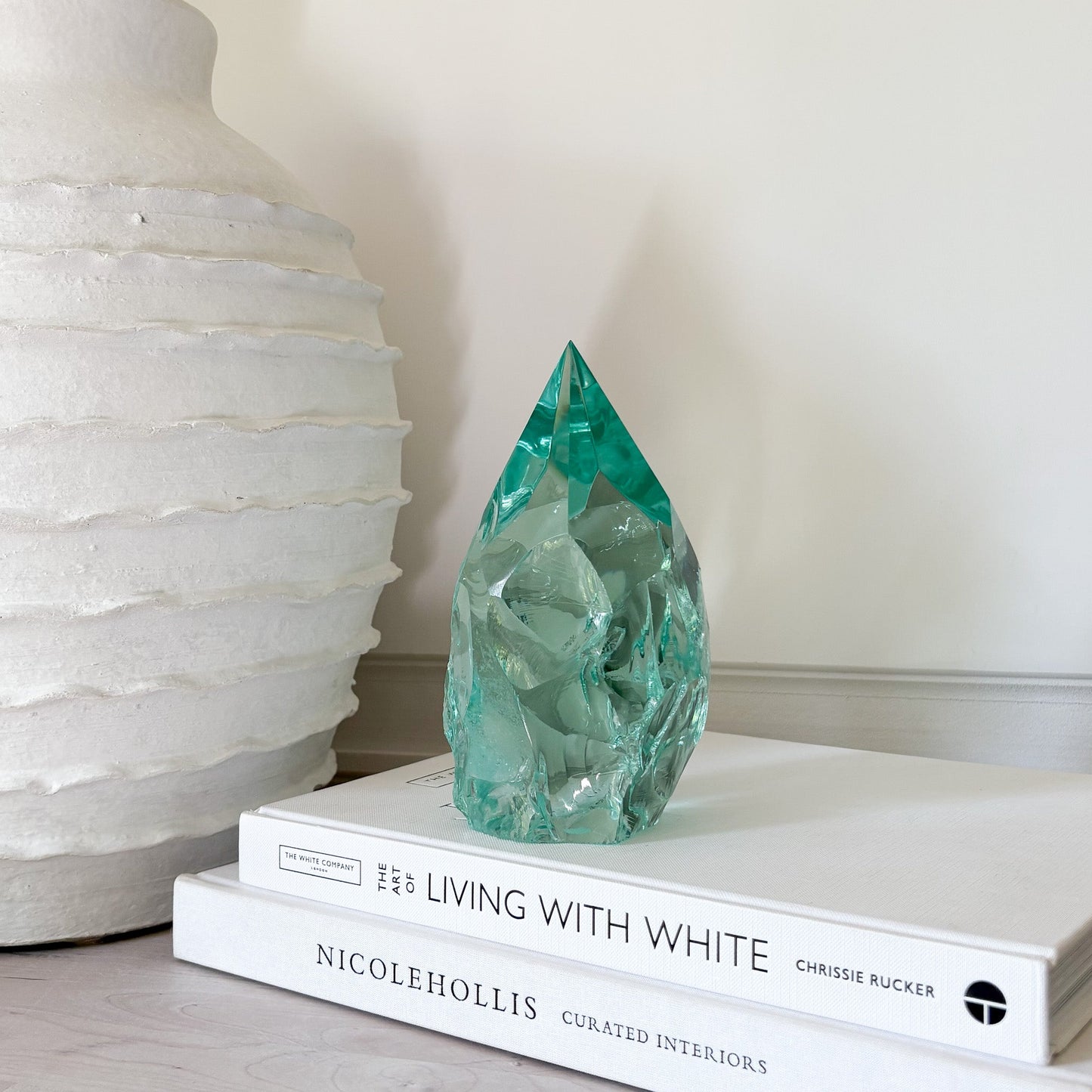 Green crystal sculpture on a stack of books with a white vase in the background