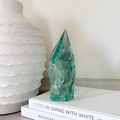 Teal glass sculpture on a stack of books with a white textured vase in the background
