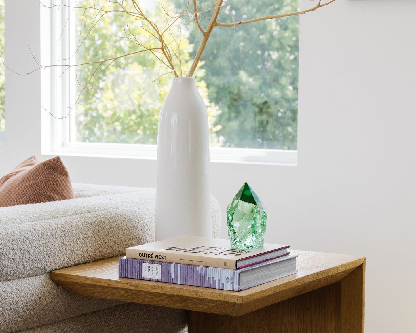 Rustic green glass point styled on books beside a white ceramic vase in a bright neutral living room