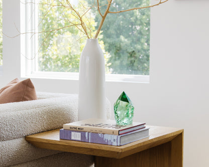 Rustic green glass point styled on books beside a white ceramic vase in a bright neutral living room