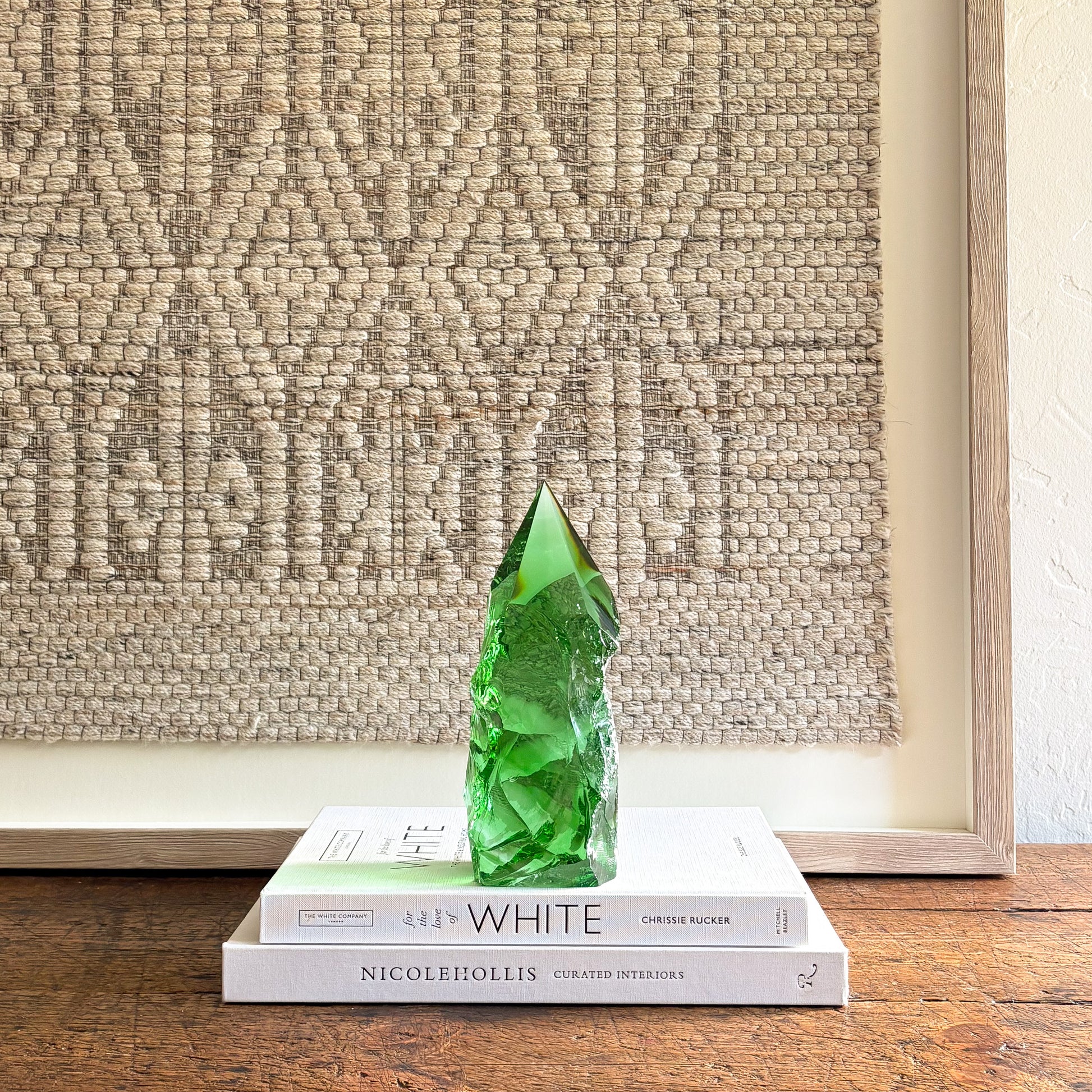 Rustic emerald green glass crystal point displayed on stacked design books with neutral woven wall backdrop