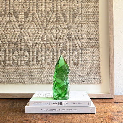Rustic emerald green glass crystal point displayed on stacked design books with neutral woven wall backdrop