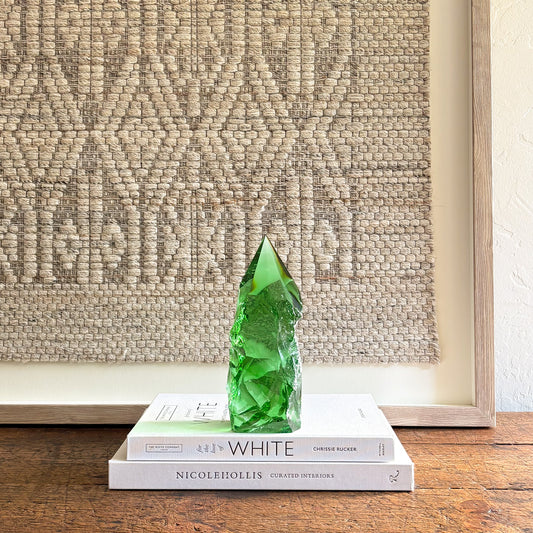 Rustic emerald green glass crystal point displayed on stacked design books with neutral woven wall backdrop
