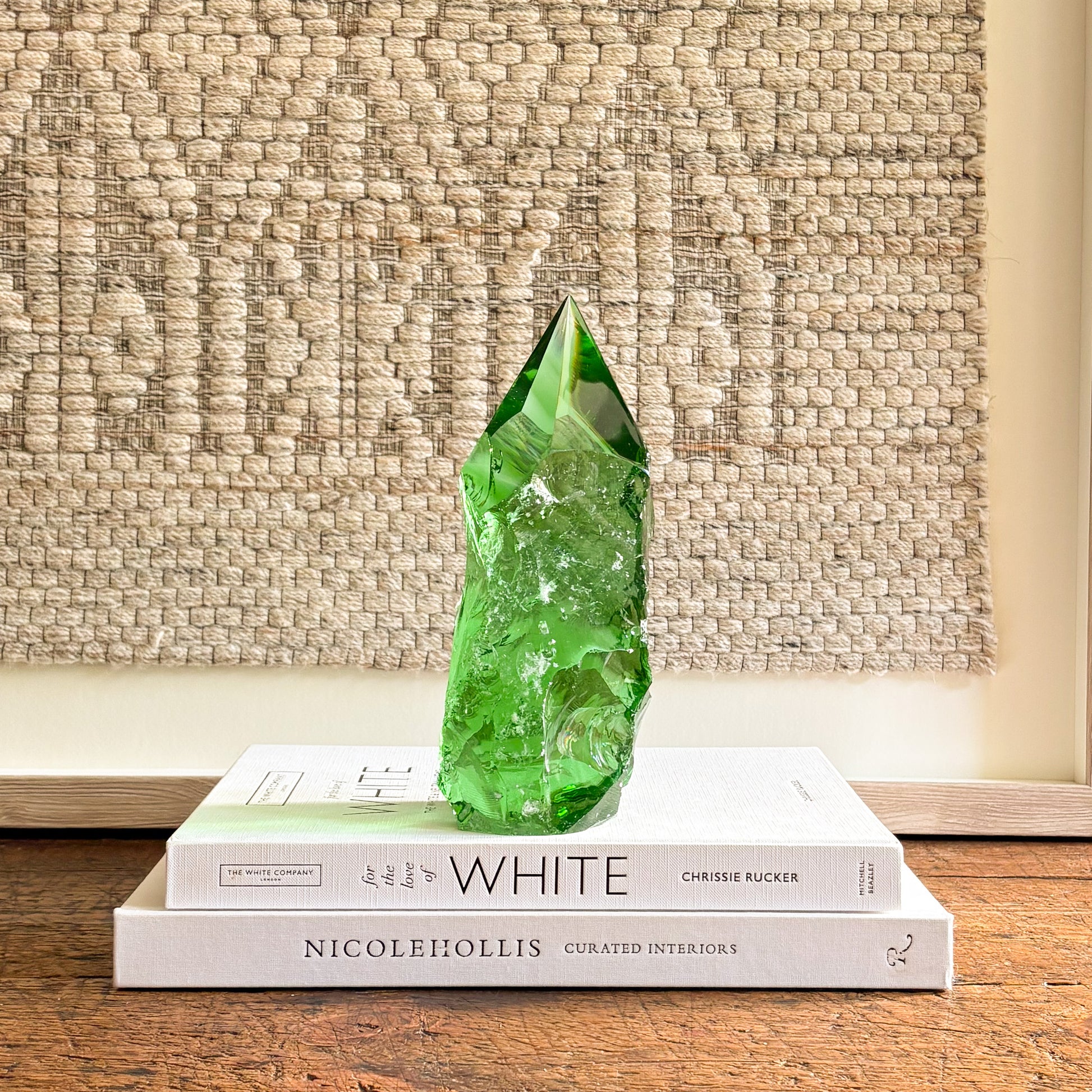Hand-cut emerald green glass crystal point styled as a modern decorative accent on design books
