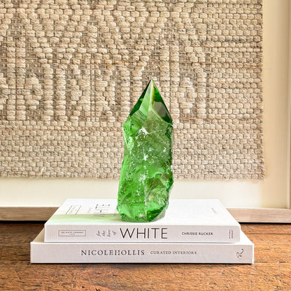 Hand-cut emerald green glass crystal point styled as a modern decorative accent on design books