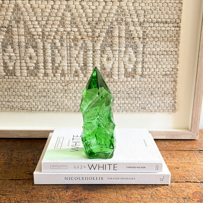 Hand-cut emerald green glass crystal point styled as a modern decorative accent on design books