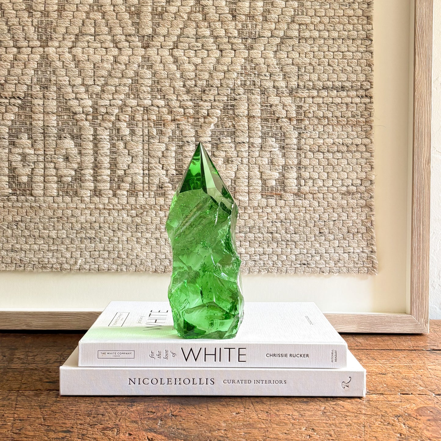 Emerald green glass crystal point with faceted tip, styled on coffee table books in a minimalist interior