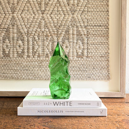 Emerald green glass crystal point with faceted tip, styled on coffee table books in a minimalist interior