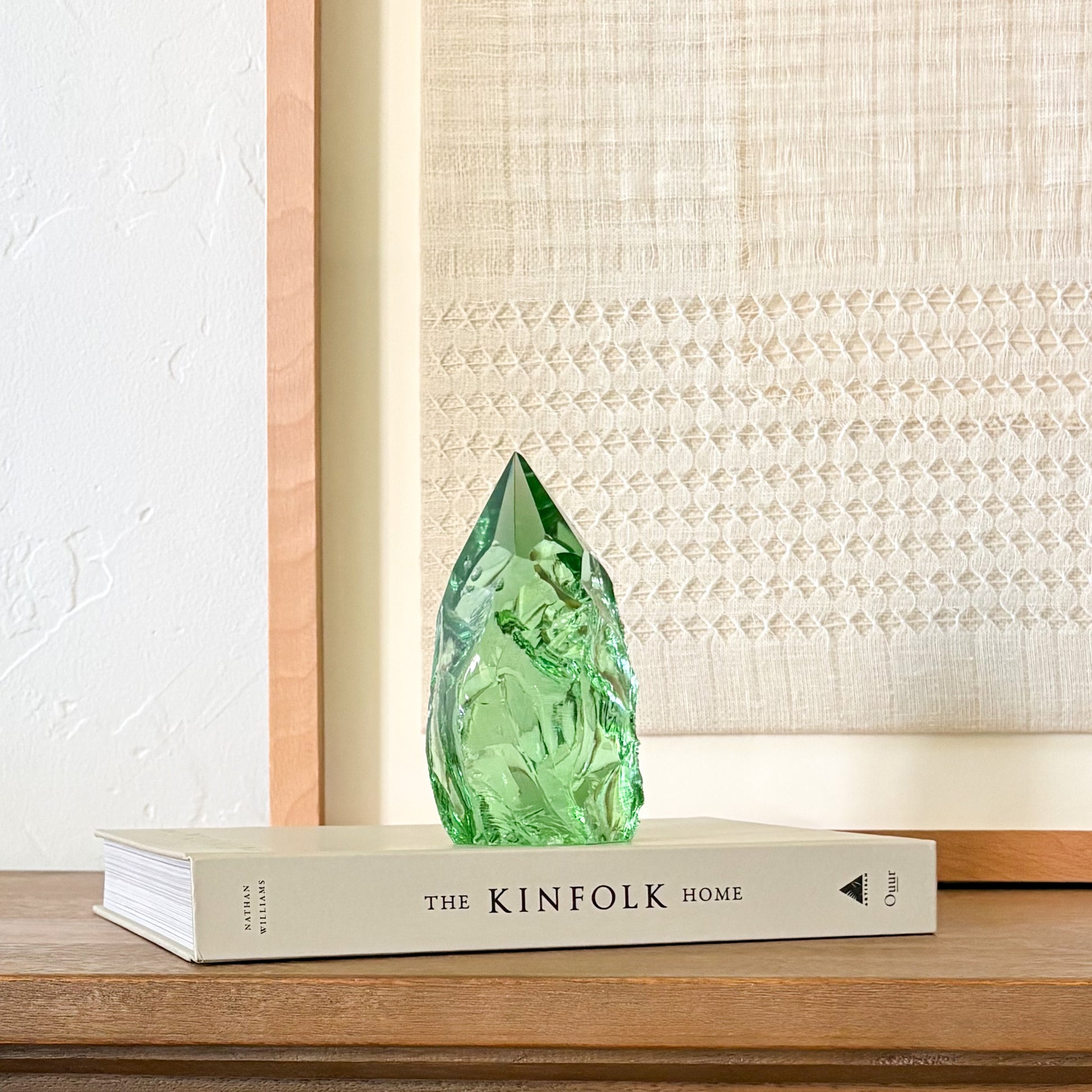 Rustic green glass crystal point displayed on Kinfolk book with neutral woven wall decor background