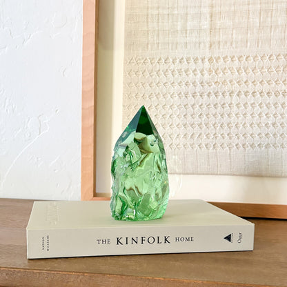 Translucent green glass point sculpture on stacked book, minimalist rustic home decor