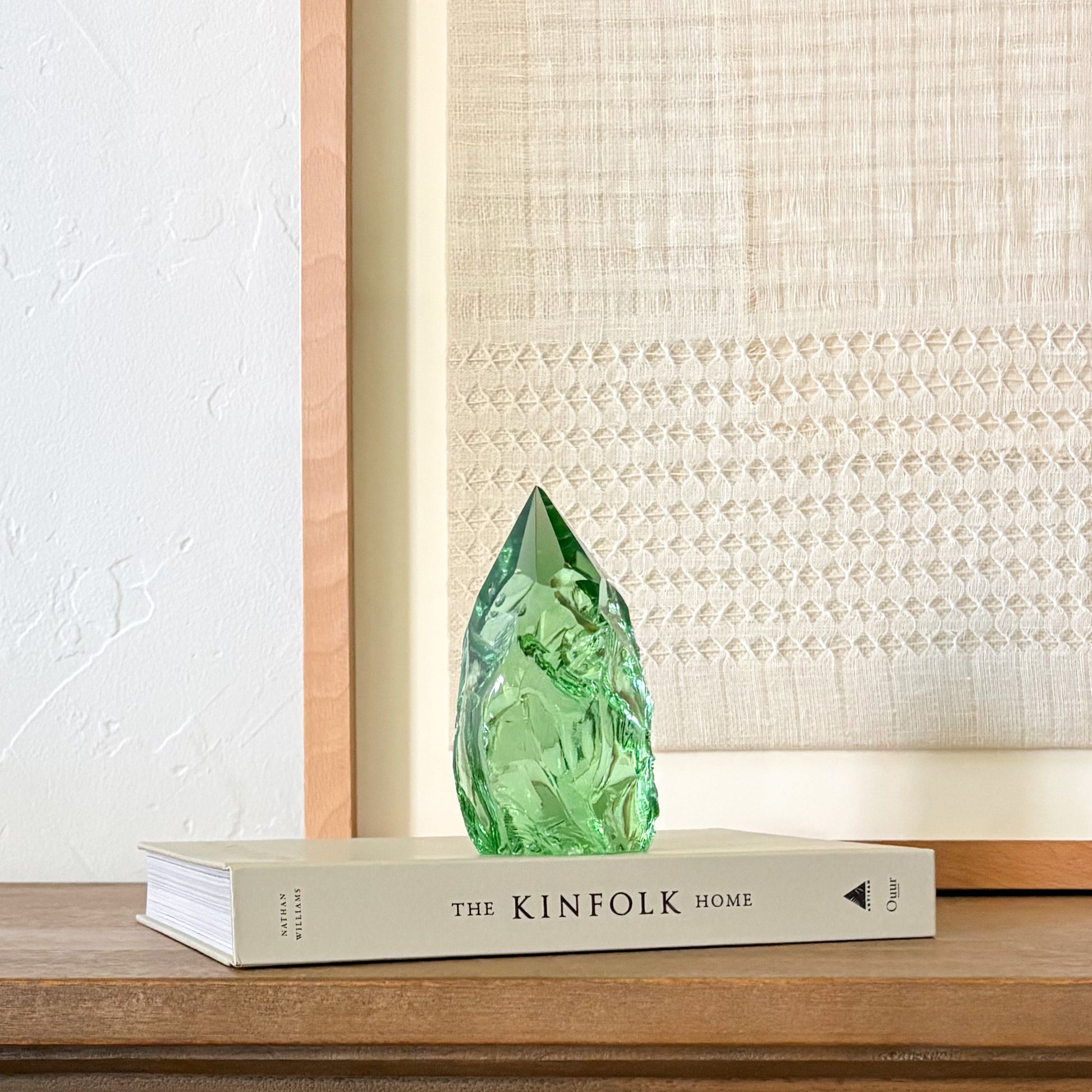 Handcrafted green glass crystal tower with natural texture on wooden shelf, modern rustic styling