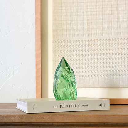 Handcrafted green glass crystal tower with natural texture on wooden shelf, modern rustic styling