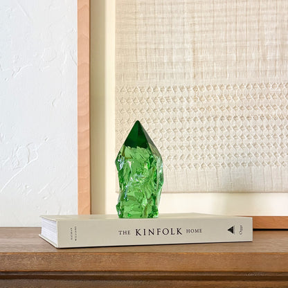 Green glass gemstone-style point on book with woven wall art, modern rustic interior