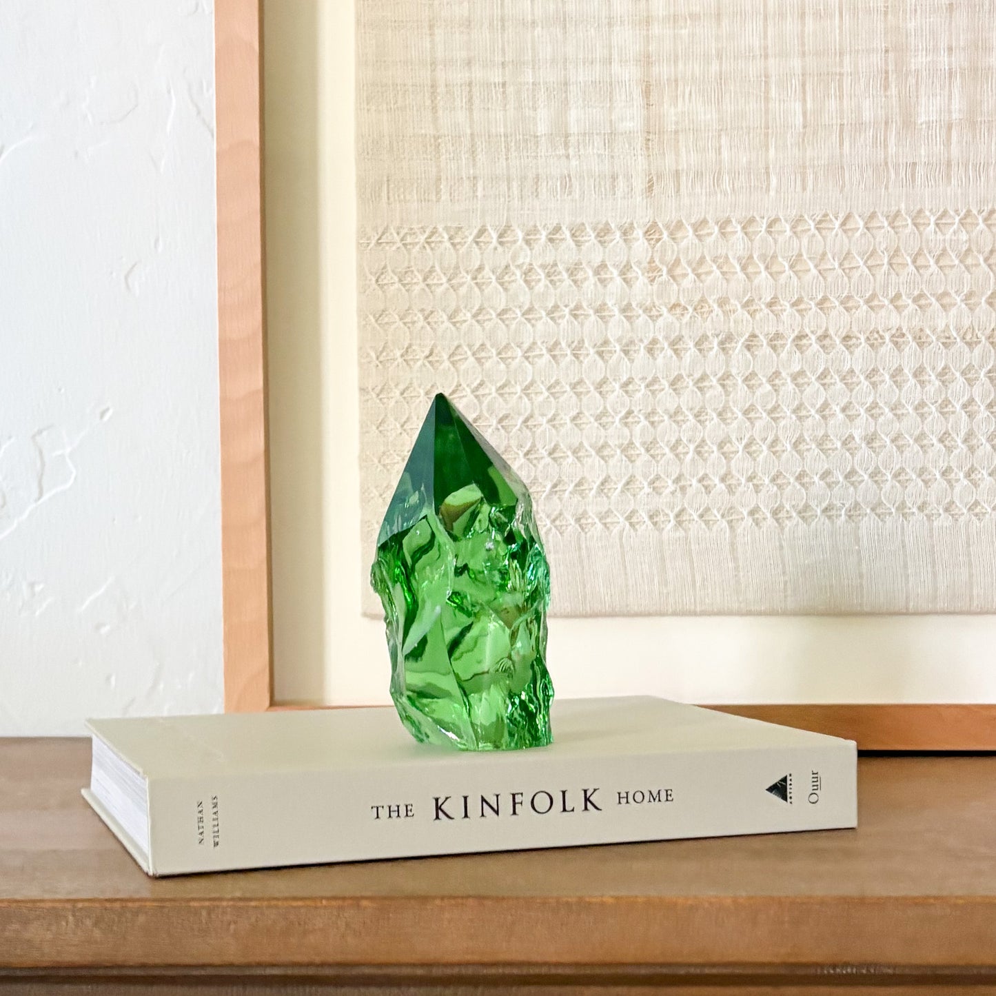Rustic green glass crystal point displayed on Kinfolk book with neutral woven wall decor background