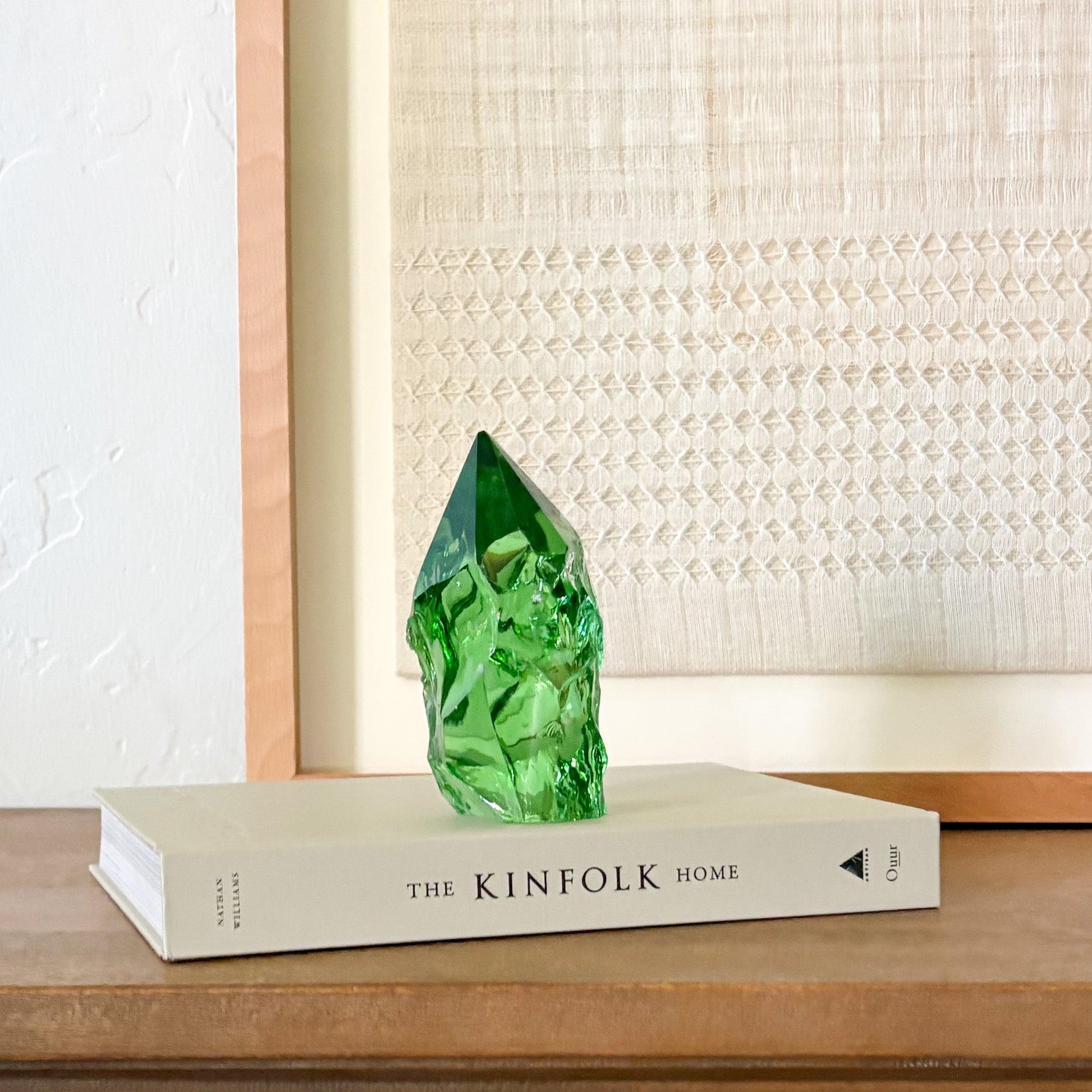 Rustic green glass crystal point displayed on Kinfolk book with neutral woven wall decor background