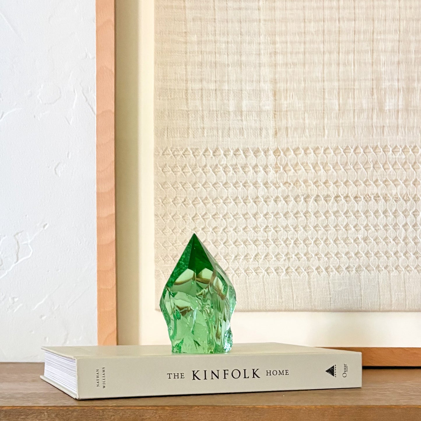 Rustic green glass crystal point displayed on Kinfolk book with neutral woven wall decor background
