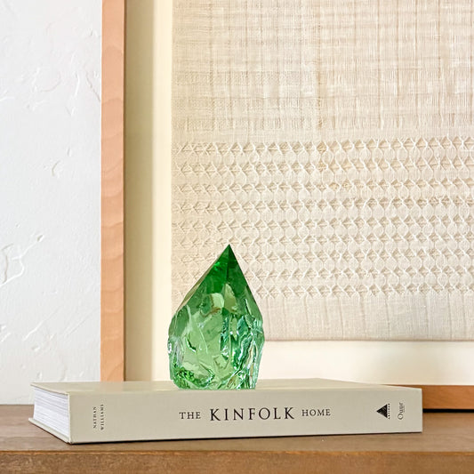 Green glass gemstone-style point on book with woven wall art, modern rustic interior