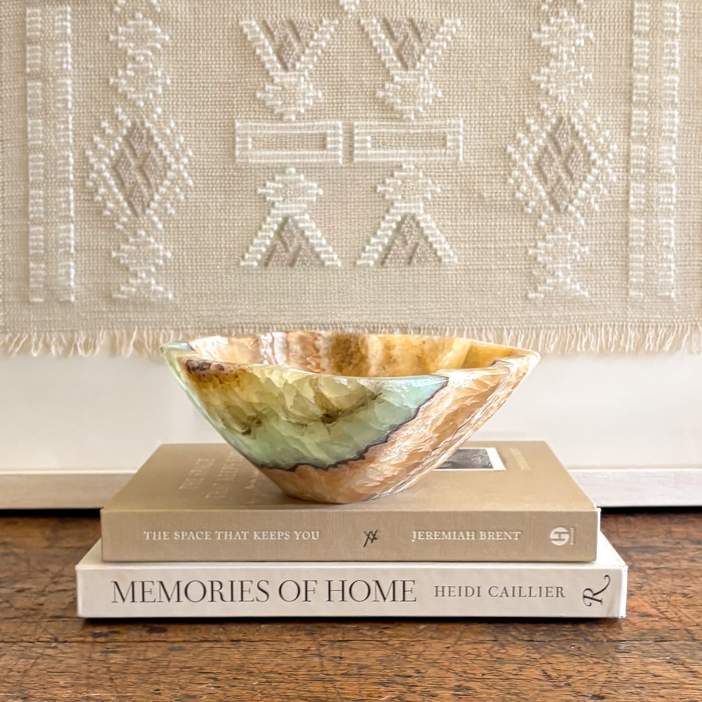 Green and honey toned serpentine onyx bowl resting on stacked books in a neutral home decor setting