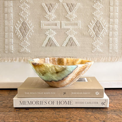 Green and honey toned serpentine onyx bowl resting on stacked books in a neutral home decor setting