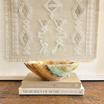 Serpentine onyx decorative bowl with green and honey veining styled on stacked books as modern home decor