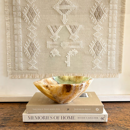 Serpentine onyx stone bowl styled on neutral books with woven textile backdrop in modern home decor