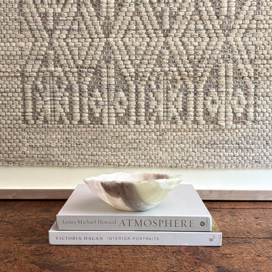Stack of books with a decorative bowl on a wooden surface against a textured wall.