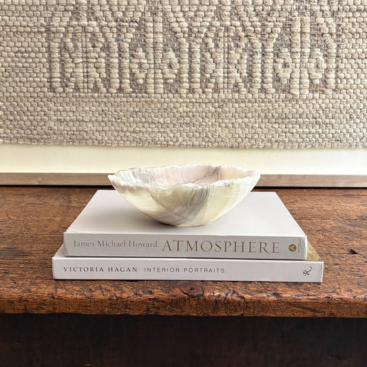 Two books stacked on a wooden surface with a decorative shell on top, against a textured wall.