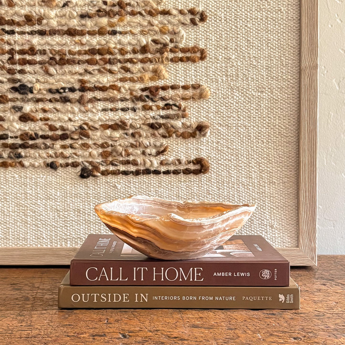 Decorative amber onyx bowl on books against a woven textured wall