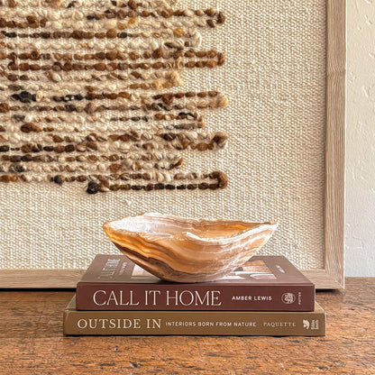Decorative amber onyx bowl on books against a woven textured wall