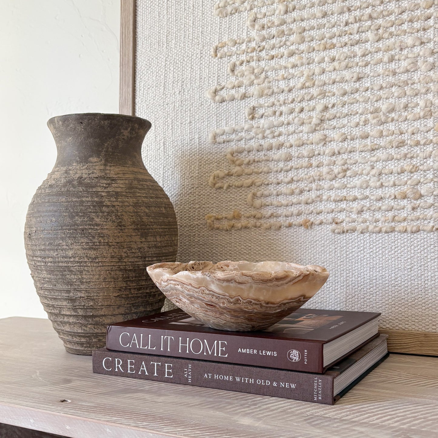 Small hand-carved amber onyx bowl displayed on stacked coffee table books in a neutral home décor setting