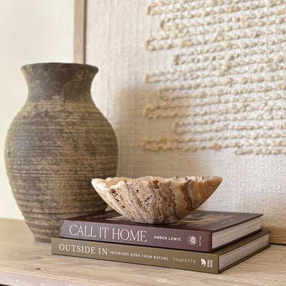 Small hand-carved amber onyx bowl displayed on stacked coffee table books in a neutral home décor setting