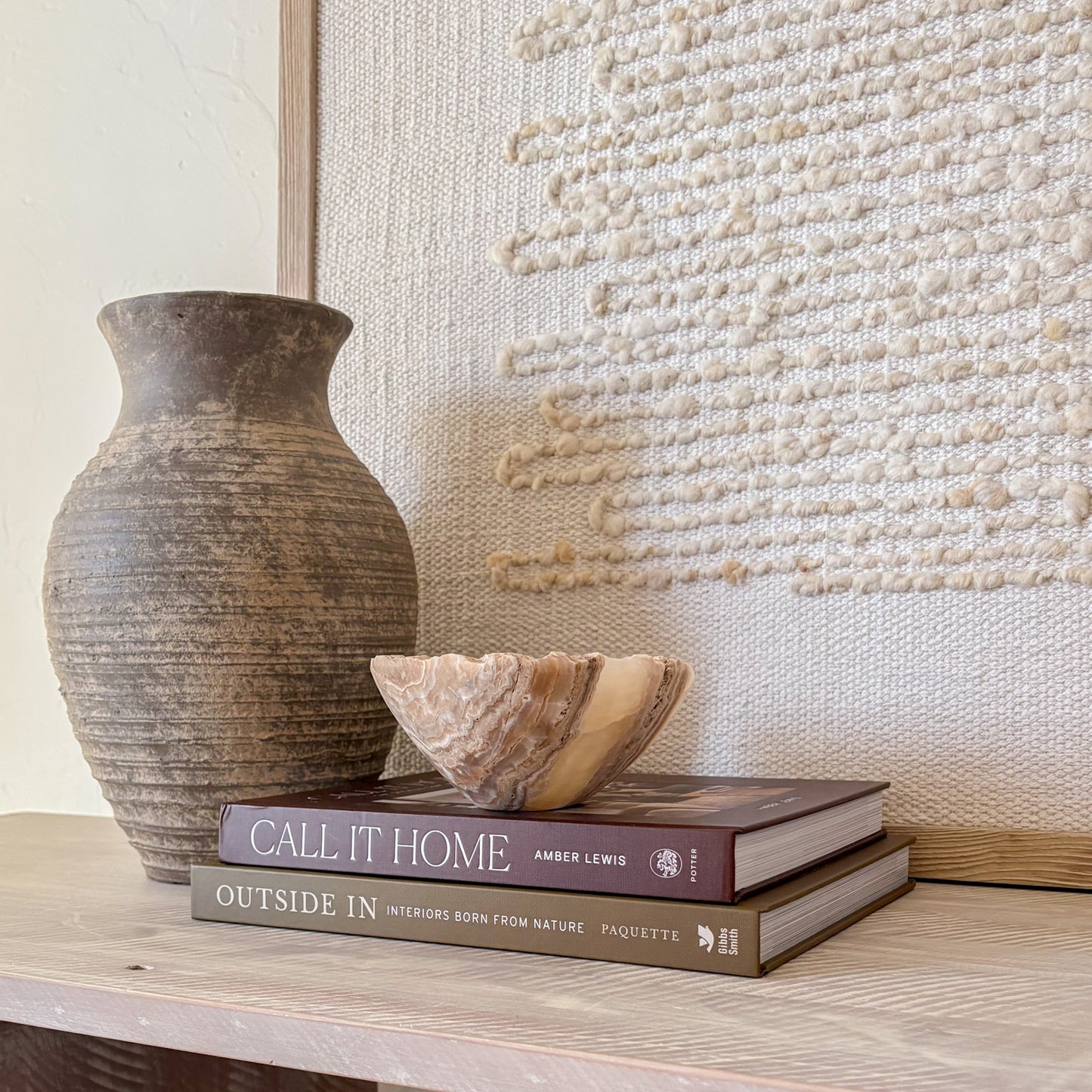 Small hand-carved amber onyx bowl displayed on stacked coffee table books in a neutral home décor setting