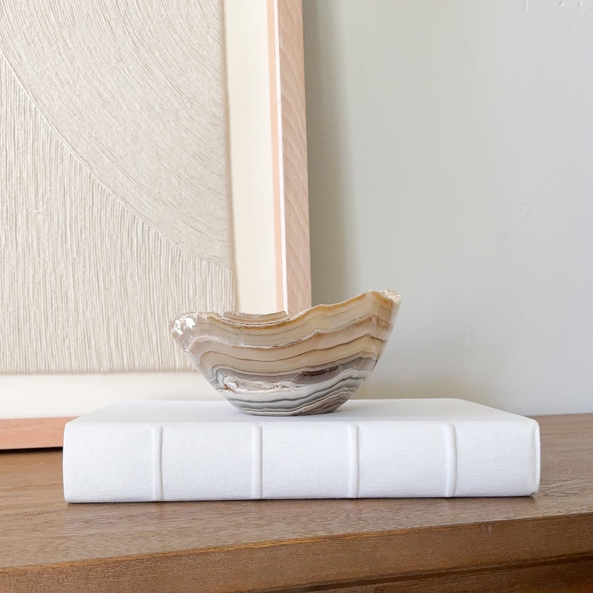 Small polished amber onyx bowl with organic wavy edge and natural striped veining, minimalist stone decor piece