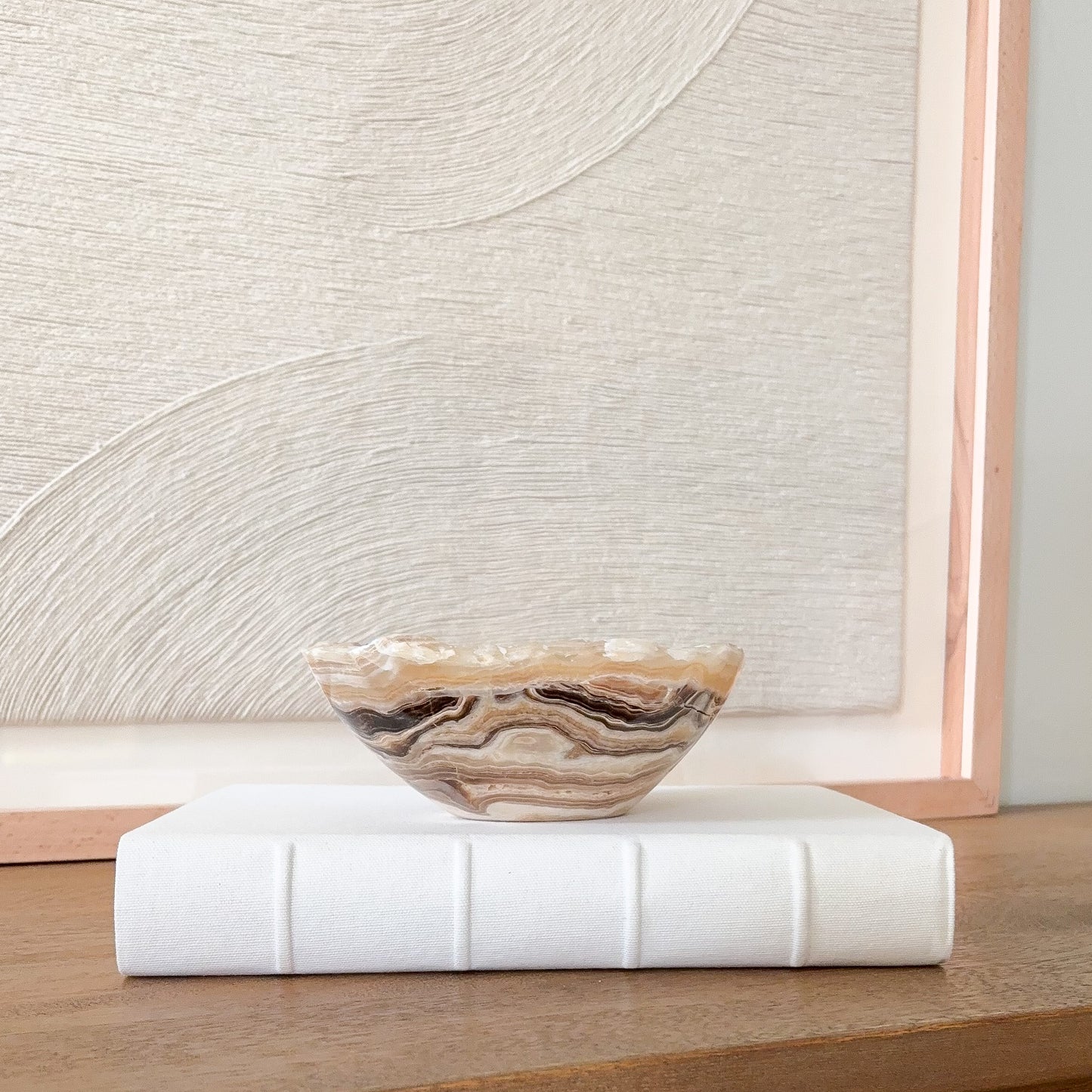 Small polished amber onyx bowl with organic wavy edge and natural striped veining, minimalist stone decor piece