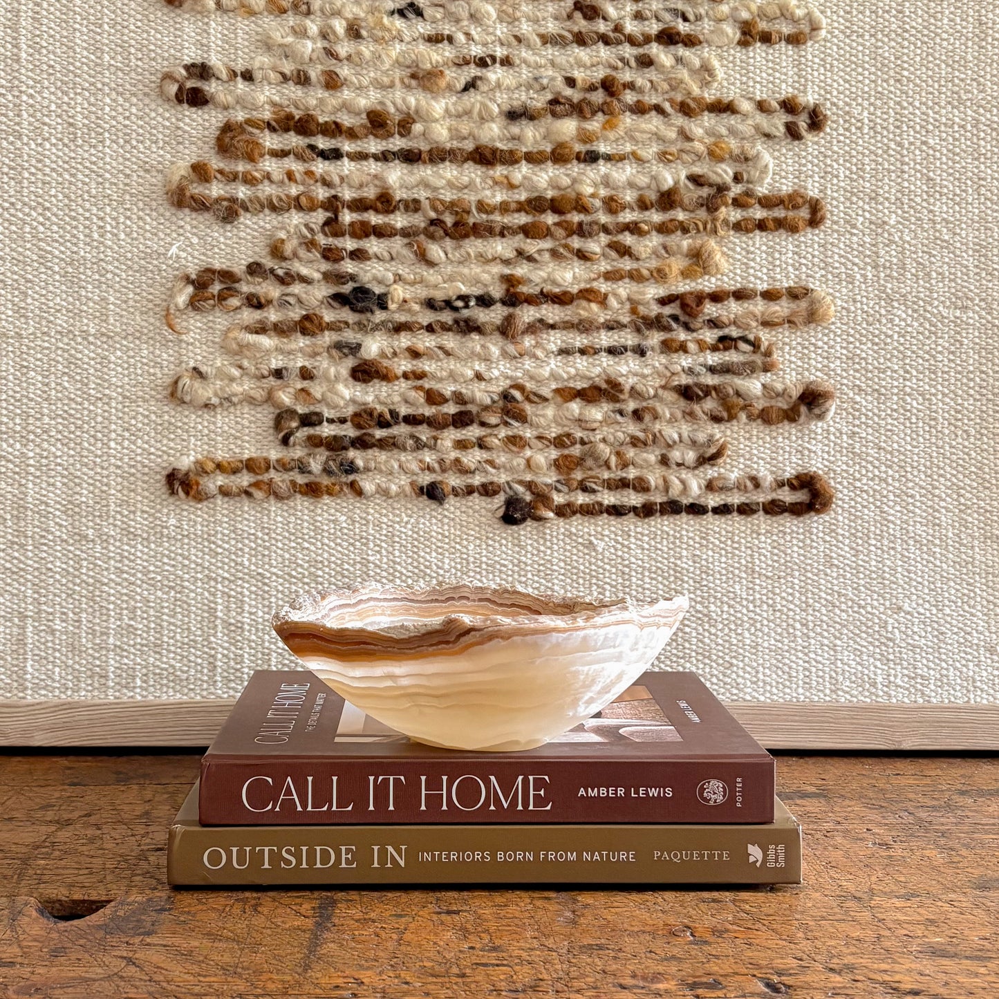 Small hand carved amber onyx bowl styled on interior design books with woven wall art background