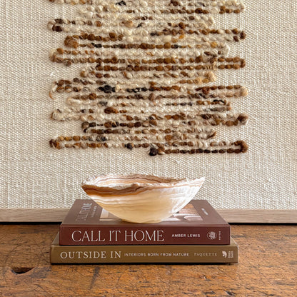 Small hand carved amber onyx bowl styled on interior design books with woven wall art background