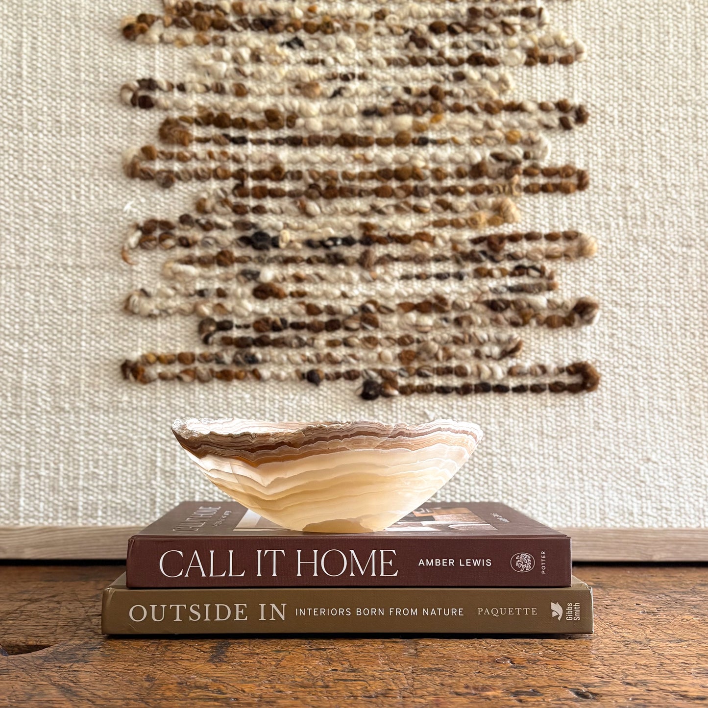 Small hand carved amber onyx bowl with layered natural stone veining displayed on stacked design books