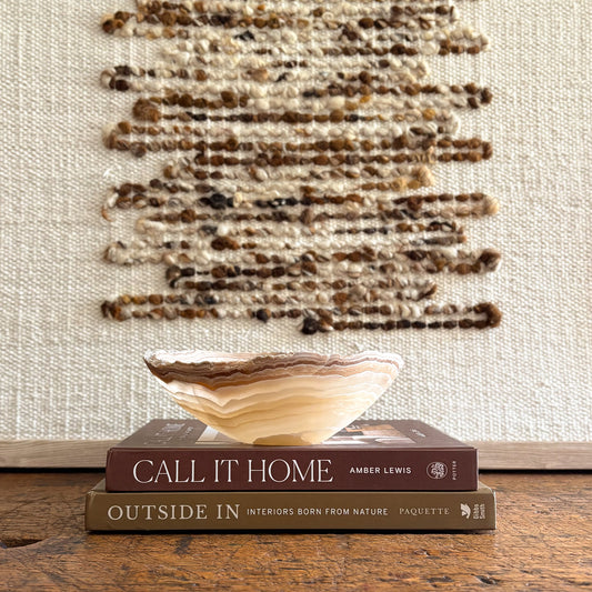 Small hand carved amber onyx bowl with layered natural stone veining displayed on stacked design books