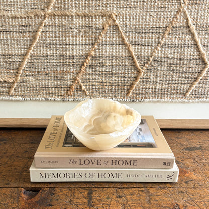 Small beige onyx bowl on top of two books titled 'The Love of Home' and 'Memories of Home' against a woven wall.