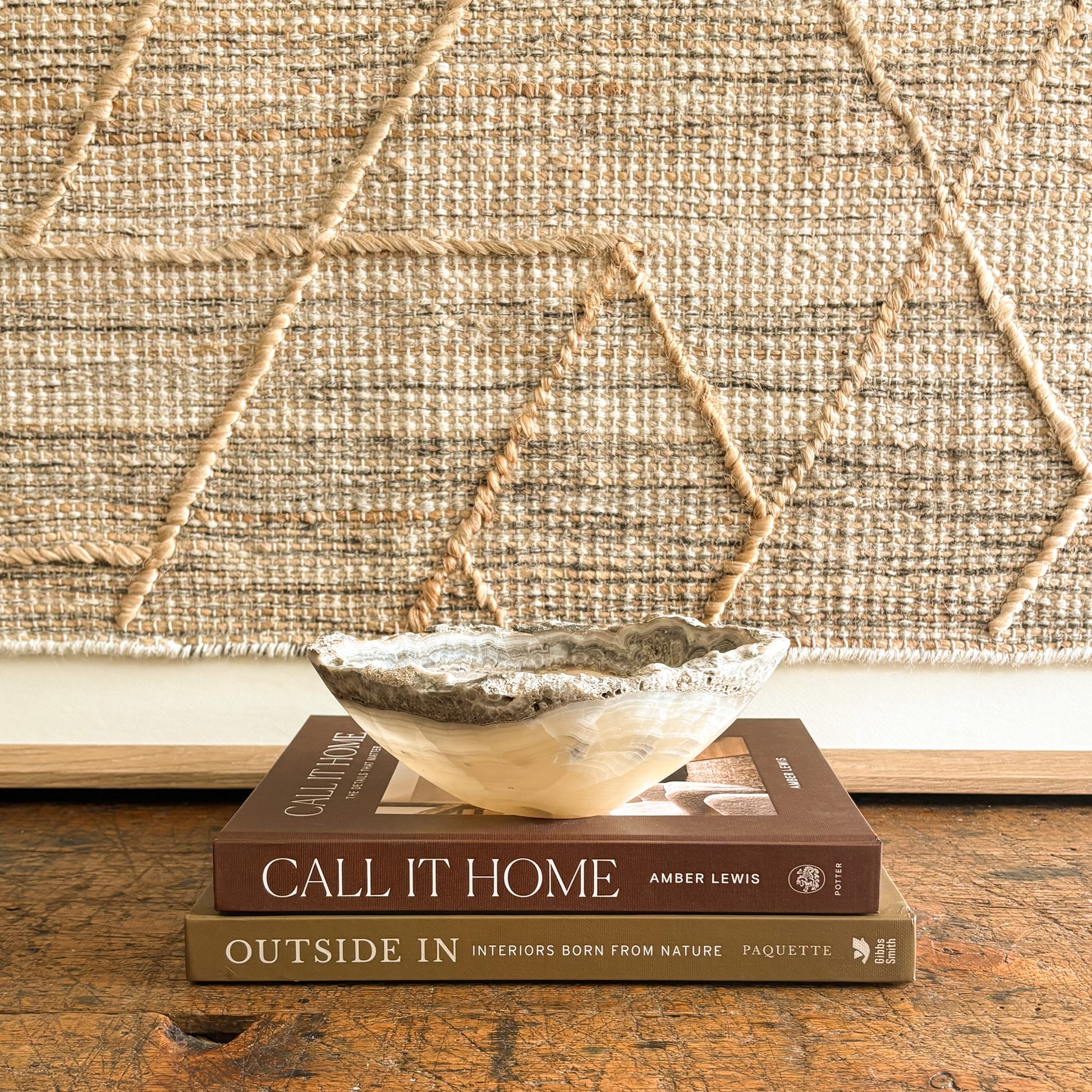 Stack of books titled 'Call It Home' and 'Outside In' with a decorative onyx bowl on top, against a textured wall.