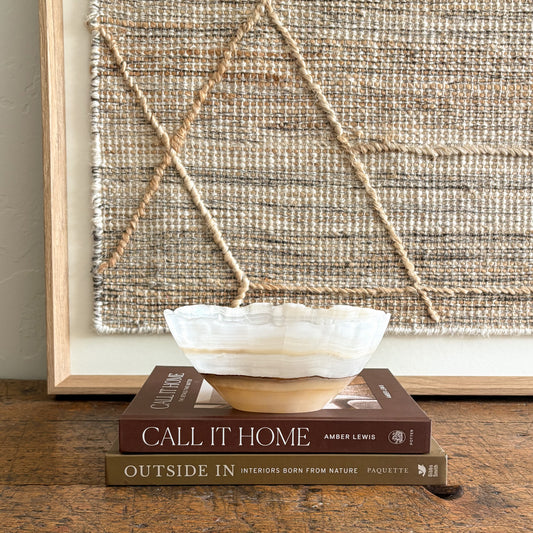 Decorative brown and white onyx bowl on books with a textured wall art piece in the background
