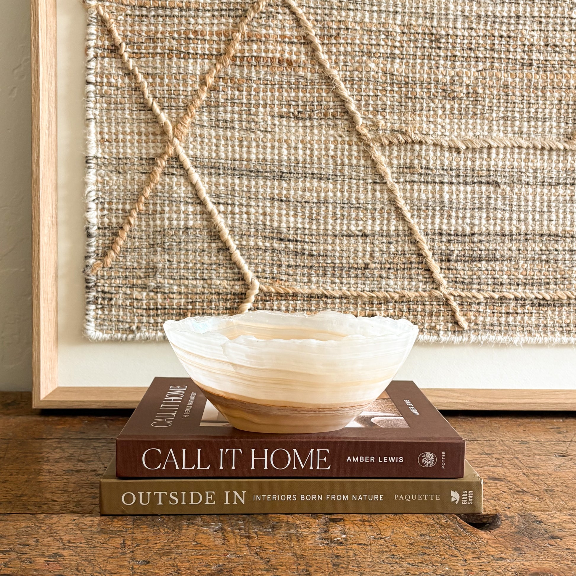 Decorative white and brown onyx bowl on books with a textured wall art piece in the background