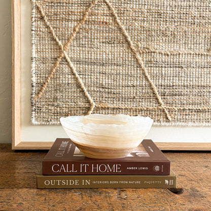 Decorative white and brown onyx bowl on books with a textured wall art piece in the background