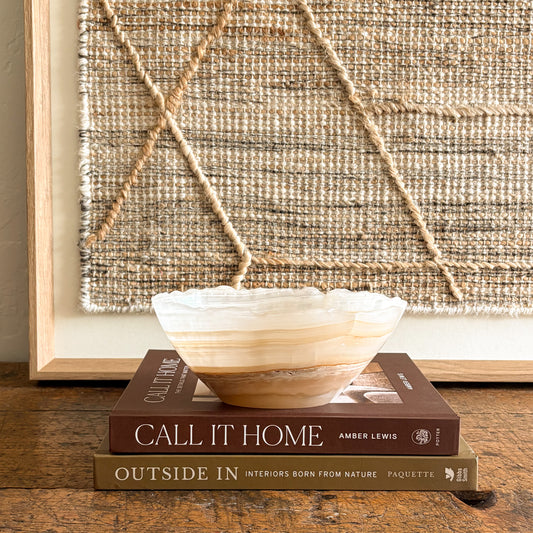 Decorative onyx bowl on books with a textured wall art in the background